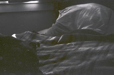 Unmade bed with rumpled sheets and pillow, minimalist interior. Soft shadows suggest natural light. Timeless domestic scene.