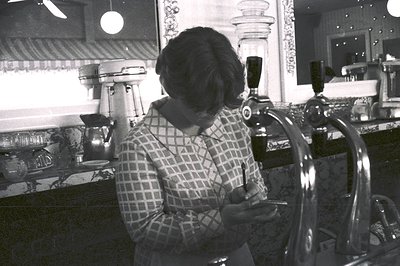 Barista operating vintage lever espresso machine in mid-20th-century café. Checkered blouse and retro bar setup with chrome t...