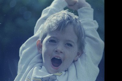 Vintage candid shot of a child laughing joyfully, arms raised, with water droplets on face and clothing. Polaroid-style grain...
