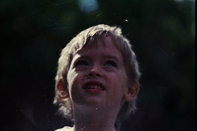 Vintage black-and-white portrait of a young girl looking upward, sunlight filtering through leaves creating lens flares. Cand...