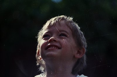 Vintage-style close-up of a child laughing under rain, droplets suspended in sunlight. Silhouetted trees frame the scene, sug...