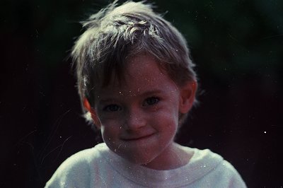 Vintage candid of a young child mid-laugh, water droplets clinging to hair and face. Soft focus and warm sepia tone suggest m...