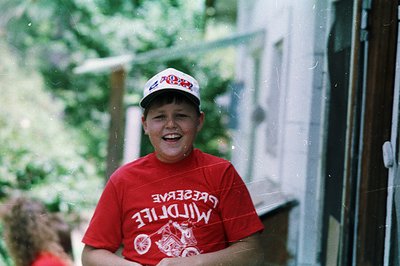 Vintage-style photo of a smiling child in a red "Preserve Wildlife" T-shirt and matching cap, likely from the 1980s–1990s. Ou...