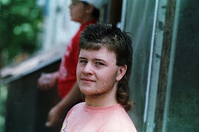 Vintage candid shot of a young person leaning against a metal railing, blurred rain droplets on lens. Subject wears a pink sh...