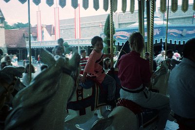 Vintage carousel with ornate wooden horses and decorative canopy. Mid-20th century amusement park setting, likely 1950s–1970s...