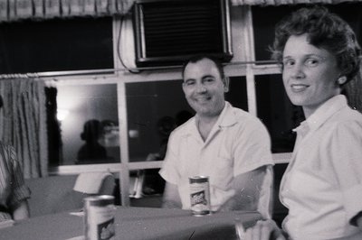 Black-and-white photo of two individuals in casual 1960s attire—man in a short-sleeve button-up, woman in a collared blouse—p...