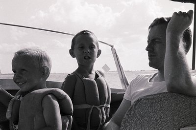 Mid-20th century black-and-white photo of three individuals on a boat, likely a family enjoying water activities. The man wea...