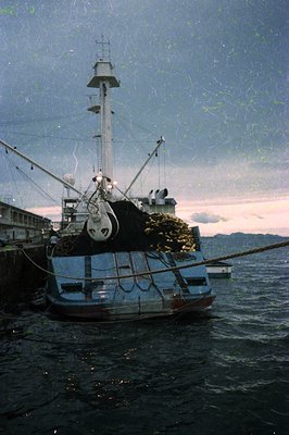 Vintage fishing vessel docked at port, loaded with large nets and ropes. Industrial-era maritime design with wooden hull and ...