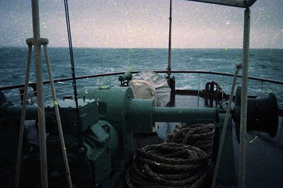 Vintage naval bridge view showing a green-painted gun turret and coiled ropes on a mid-20th century warship. Open horizon and...