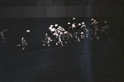 Vintage black-and-white football huddle under stadium lights, showcasing classic helmet designs and numbered jerseys. Dynamic...
