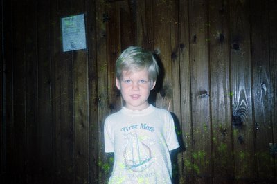 Young boy in a vintage "First Mate" nautical-themed T-shirt poses against a weathered wooden fence. The faded print suggests ...