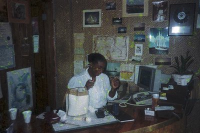 Vintage office interior featuring a seated individual in a white shirt, holding a drink and gesturing. Decor includes framed ...