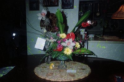 Vintage floral arrangement on a mosaic tabletop, featuring red, yellow, and white blooms with green foliage. A small figurine...