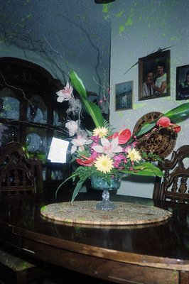 Vintage floral arrangement in a blue glass vase on a curved wooden table, featuring orchids, daisies, and greenery. Wooden ca...