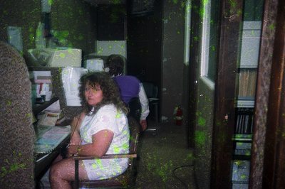 Vintage office interior with two women seated at desks, likely 1980s–1990s. One woman wears a floral blouse; the other, a str...