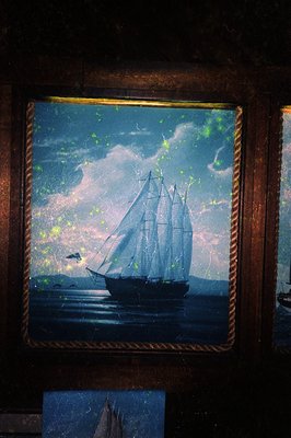 Vintage maritime painting framed in distressed wood, depicting a classic schooner under stormy skies with golden flecks. Refl...