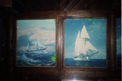 Vintage framed maritime paintings depicting a sailing ship in stormy seas (left) and a classic schooner under moonlight (righ...