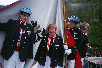 Uniformed group in traditional alpine attire poses under a tent, likely for a cultural festival or historical reenactment. Me...