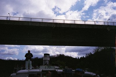 Vintage black-and-white photo of a man in a white uniform standing atop a 1970s-era canal boat, labeled "10-11" with a cylind...