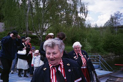 Vintage outdoor gathering featuring elderly individuals in traditional red-and-white striped folkwear, likely Finnish or Kare...