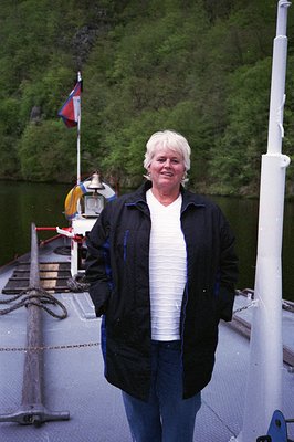 Vintage ferry deck scene featuring a woman in casual 1980s attire—striped shirt, dark jacket, and jeans—standing beside a lif...