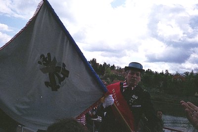 Veteran in traditional WWII-era uniform holding a large American flag, likely from a parade or memorial event. Note the "Viet...