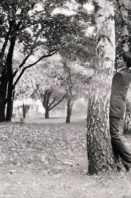 A man in mid-1900s attire (vest, tie, trousers) holds a child mid-air under a tree in a park-like setting. Soft focus backgro...