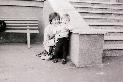 Vintage black-and-white photo of a woman holding a toddler on concrete steps, likely 1970s–1980s. Urban setting with concrete...