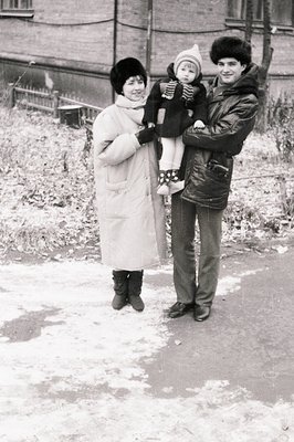 Family portrait in winter attire, likely 1960s–1970s. Woman in voluminous coat, man in leather jacket with high-waisted trous...
