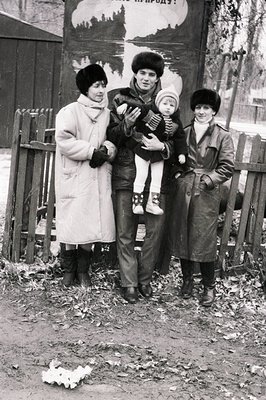 Family portrait in winter attire, likely Eastern Bloc region, 1960s–1970s. Three adults pose with a child, standing on a dirt...