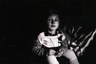 Vintage black-and-white portrait of a child indoors, holding a stuffed animal. Soft focus and grainy texture suggest mid-20th...