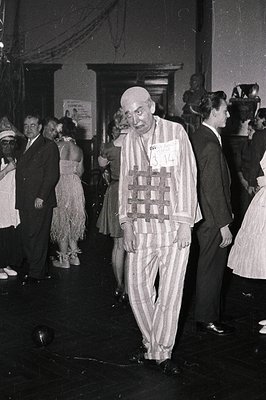 Mid-20th century black-and-white photo of a man in a striped concentration camp uniform, likely from the 1940s–1950s. Crowd i...