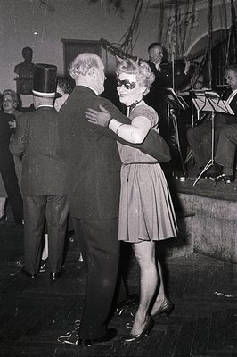 Couple dancing in a 1950s ballroom setting, men in suits with top hats, women in knee-length dresses. Orchestra with sheet mu...