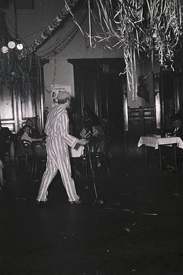 Mid-century jazz pianist in striped suit performs in dimly lit, festive venue. Decorative paper chains and vintage signage ("...