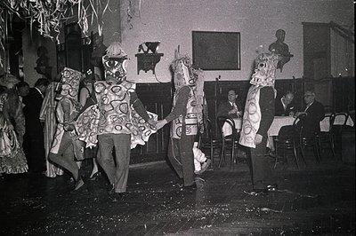 Vintage black-and-white photo of masked performers in elaborate, ornate costumes resembling mythical or folkloric figures, li...