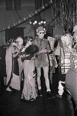 Vintage black-and-white photo of a theatrical or costume event, likely from the 1960s–70s. Central figure wears a futuristic,...