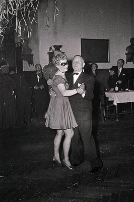 Couple dancing in a 1950s-style ballroom, framed by festive streamers. Woman in a fitted dress with a mask, man in a tuxedo. ...