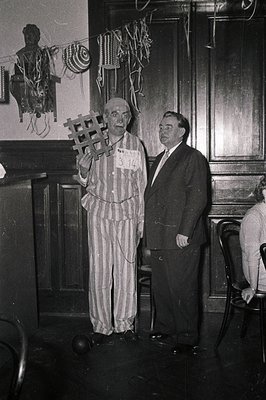 A man in a striped prisoner uniform () stands holding a wooden cross in an indoor setting, likely a 1960s-70s public event or...