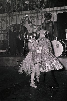 Vintage black-and-white stage performance featuring two performers in elaborate, theatrical costumes—one in a grass skirt wit...