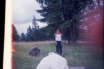Vintage photo of two men in a grassy field, likely mid-20th century. One man stands holding a fishing rod, while another knee...