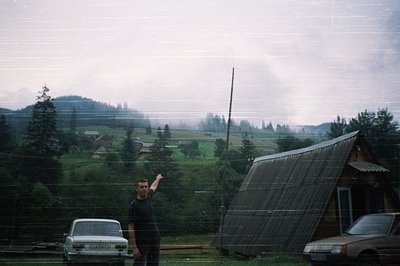 Vintage alpine village scene with man pointing toward sloped solar panel structure. Mid-20th century rural architecture and c...