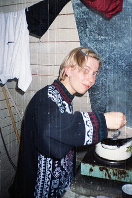 Vintage indoor shot of a person in a cozy, patterned sweater near a vintage stove. White-tiled wall and hanging laundry sugge...