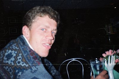 Vintage candid shot of a man in a patterned sweater, holding a fork with flowers, blurred background suggests motion or low-l...