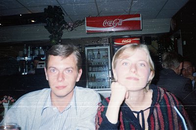 Vintage bar scene with two individuals posing for a camera. The man wears a light-colored button-up shirt, while the woman in...