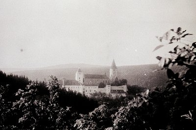 Historic castle perched atop a hill, surrounded by dense foliage. Gothic-style architecture with tall towers and crenellated ...