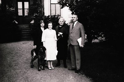 Four individuals pose outdoors in 1940s-era attire, likely post-WWII. Woman in white dress holds bouquet; man in suit holds f...