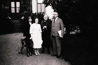 Four individuals pose outdoors in front of a grand, two-story house with classical architecture, likely mid-20th century (194...