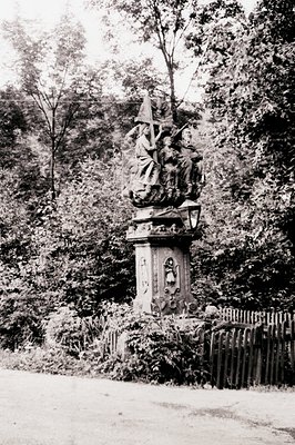 Neoclassical stone monument featuring a central relief sculpture of a robed figure holding a cross, flanked by two winged ang...