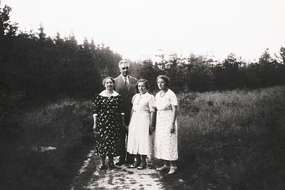 Black-and-white family portrait from the early-to-mid 20th century, likely 1930s–1940s. Four individuals pose outdoors on a g...