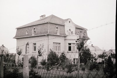 Two-story residential building with gabled roof and arched windows, likely mid-20th century. Architectural style suggests Eur...